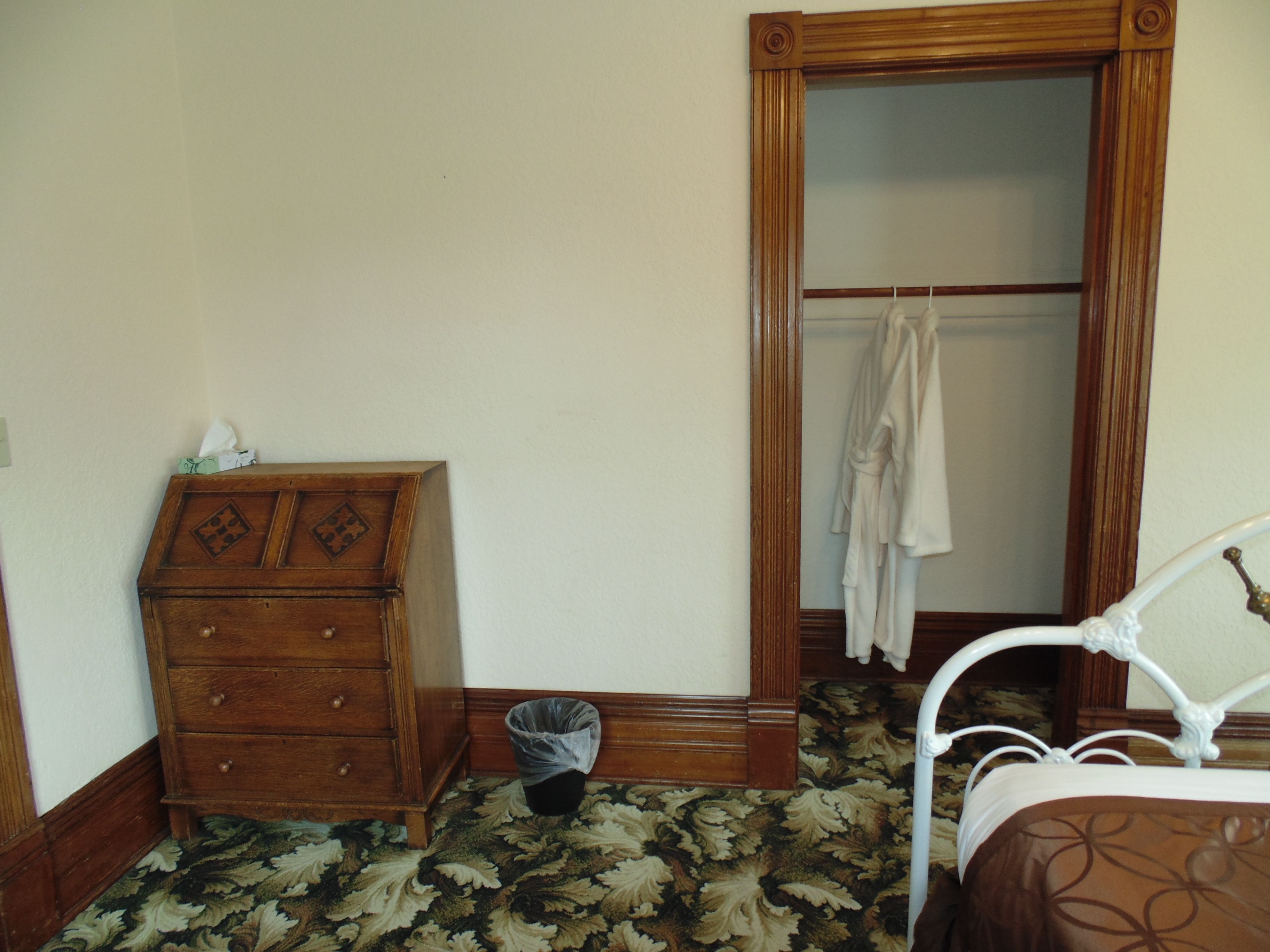 A bedroom with a wooden dresser, a metal bed frame, a patterned carpet, and a wooden wardrobe.