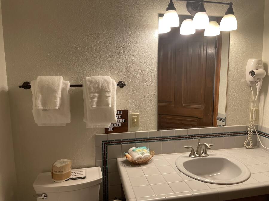 Ein Badezimmer mit Waschbecken, Spiegel, Handtuchhalter und einem Schild, das den Standort des Badezimmers anzeigt.