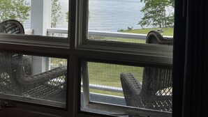 A view from inside a room with a large window overlooking a body of water, a grassy area, and a white building structure. - High Tide Inn (Camden)