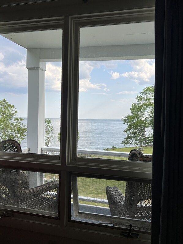 A view from inside a room with a large window overlooking a body of water, a grassy area, and a white building structure. - High Tide Inn (Camden)