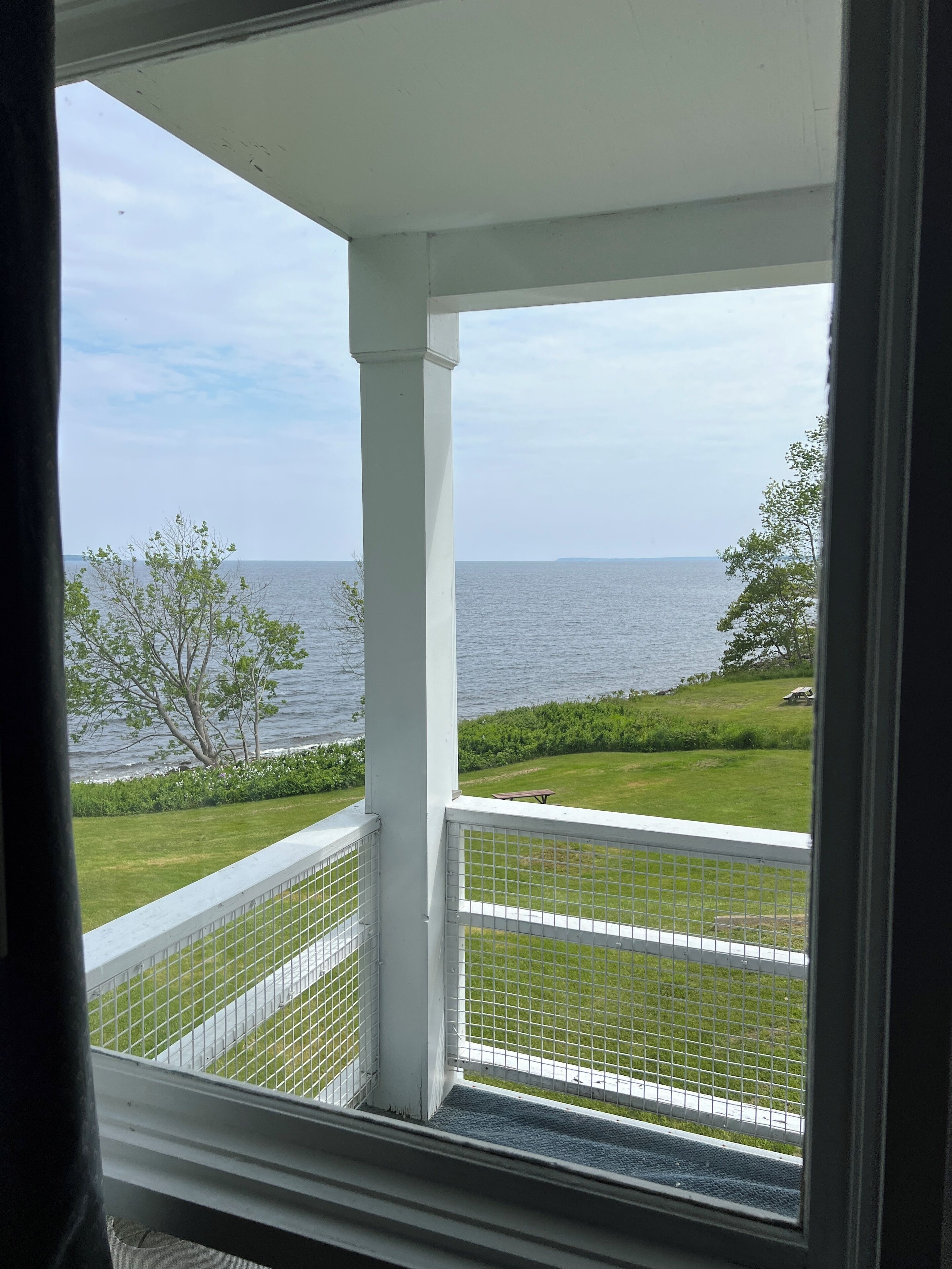A balcony with a view of the sea, a grassy lawn, and a fence.