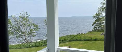 A balcony with a view of the sea, a grassy lawn, and a fence.