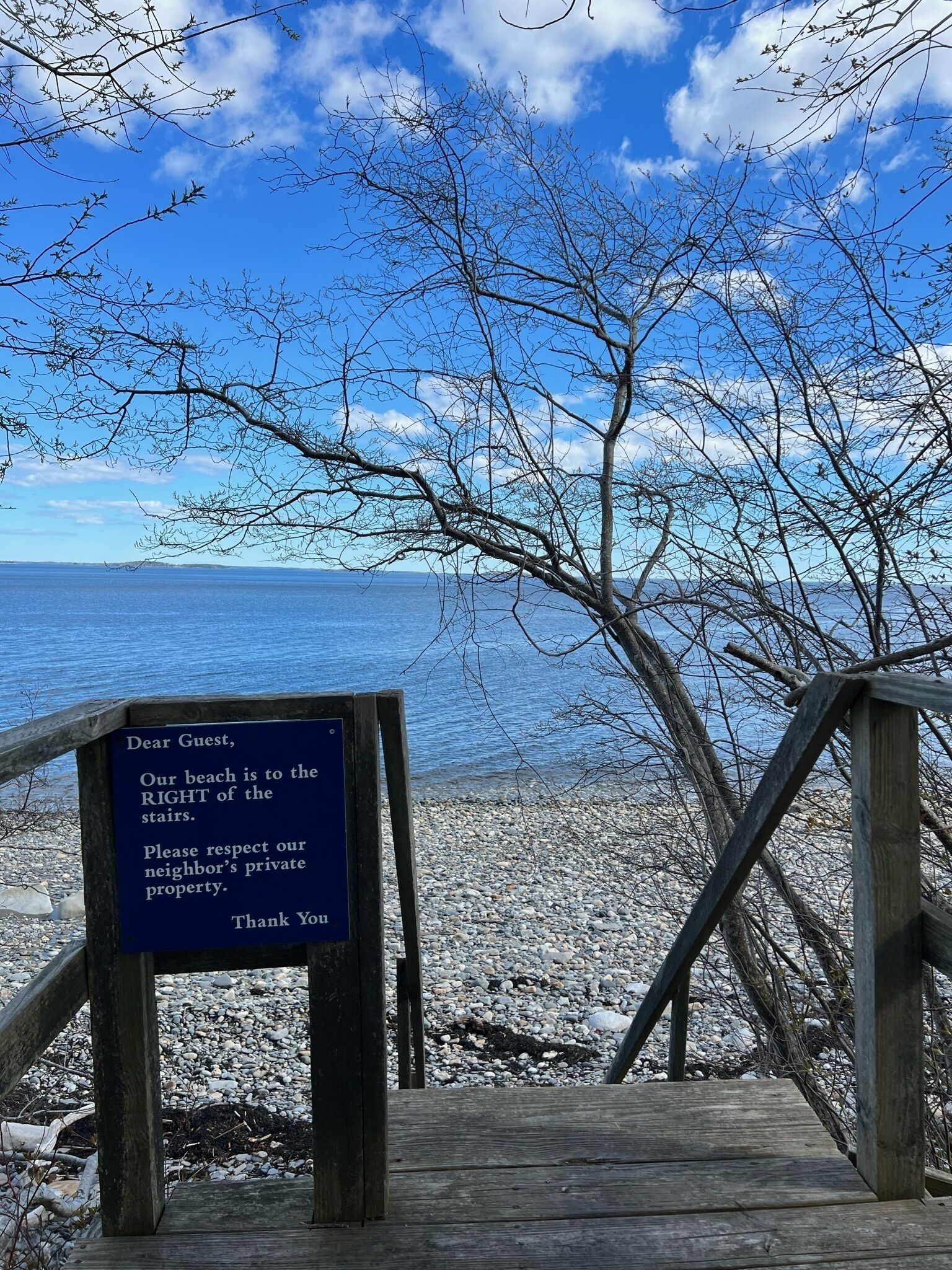 Une promenade en bois mène à une plage, et un panneau indique que la plage se trouve à droite des escaliers.