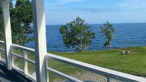 A covered outdoor area with a view of the sea, a grassy area, and a white fence. - High Tide Inn (Camden)