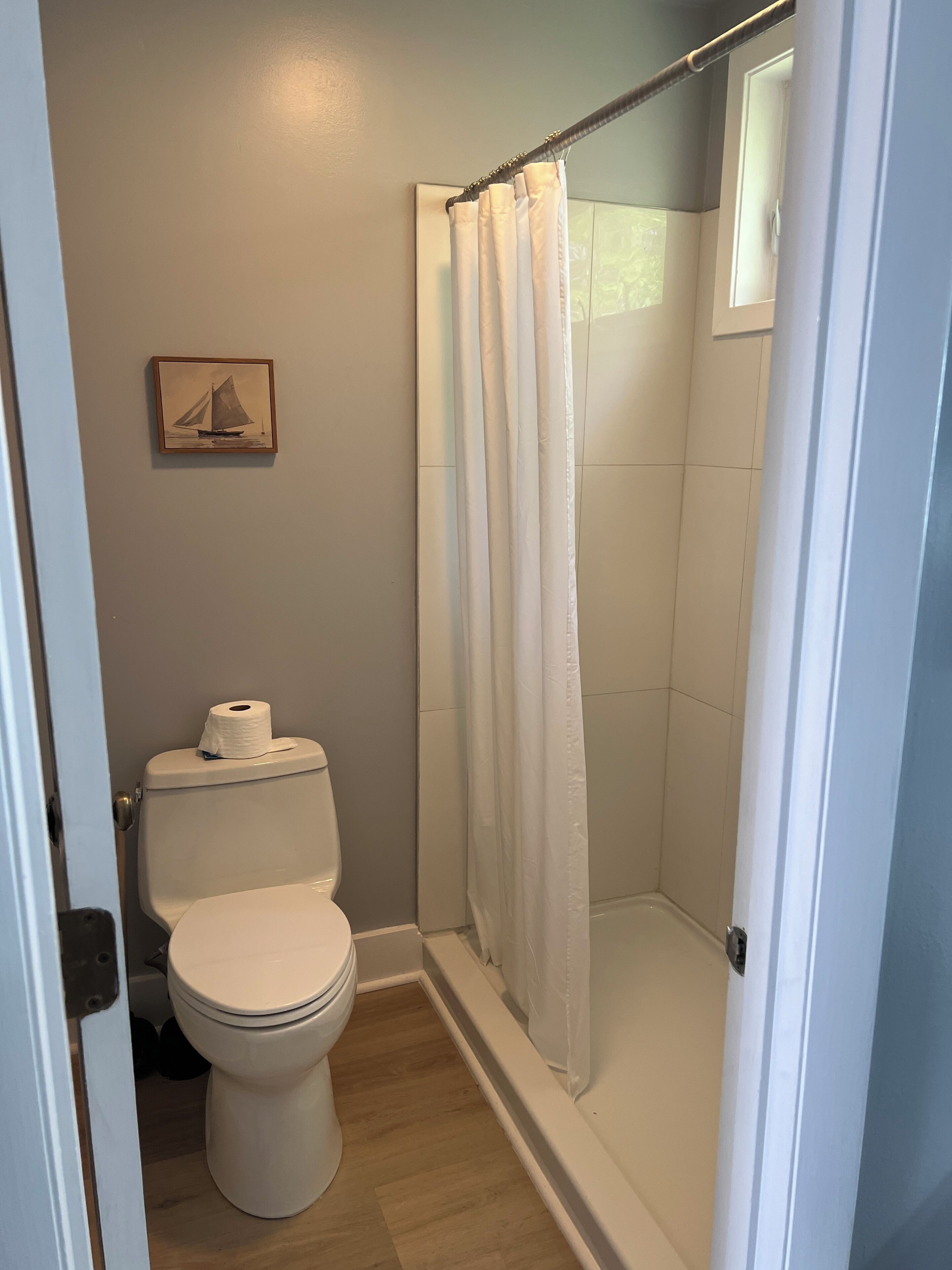 Une salle de bain avec des toilettes, une douche avec un rideau blanc et un tableau encadré au mur.