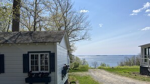 A white cabin with a window and a small porch area, situated next to a gravel path leading to a body of water. - High Tide Inn (Camden)