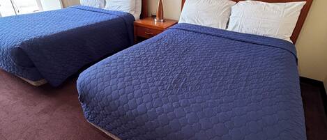 A hotel room with two beds, a wooden headboard, a nightstand with a lamp, and a framed picture on the wall.