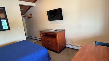 Een kamer met een bed, een bureau, een stoel, een aan de muur bevestigde televisie en een houten plafond.