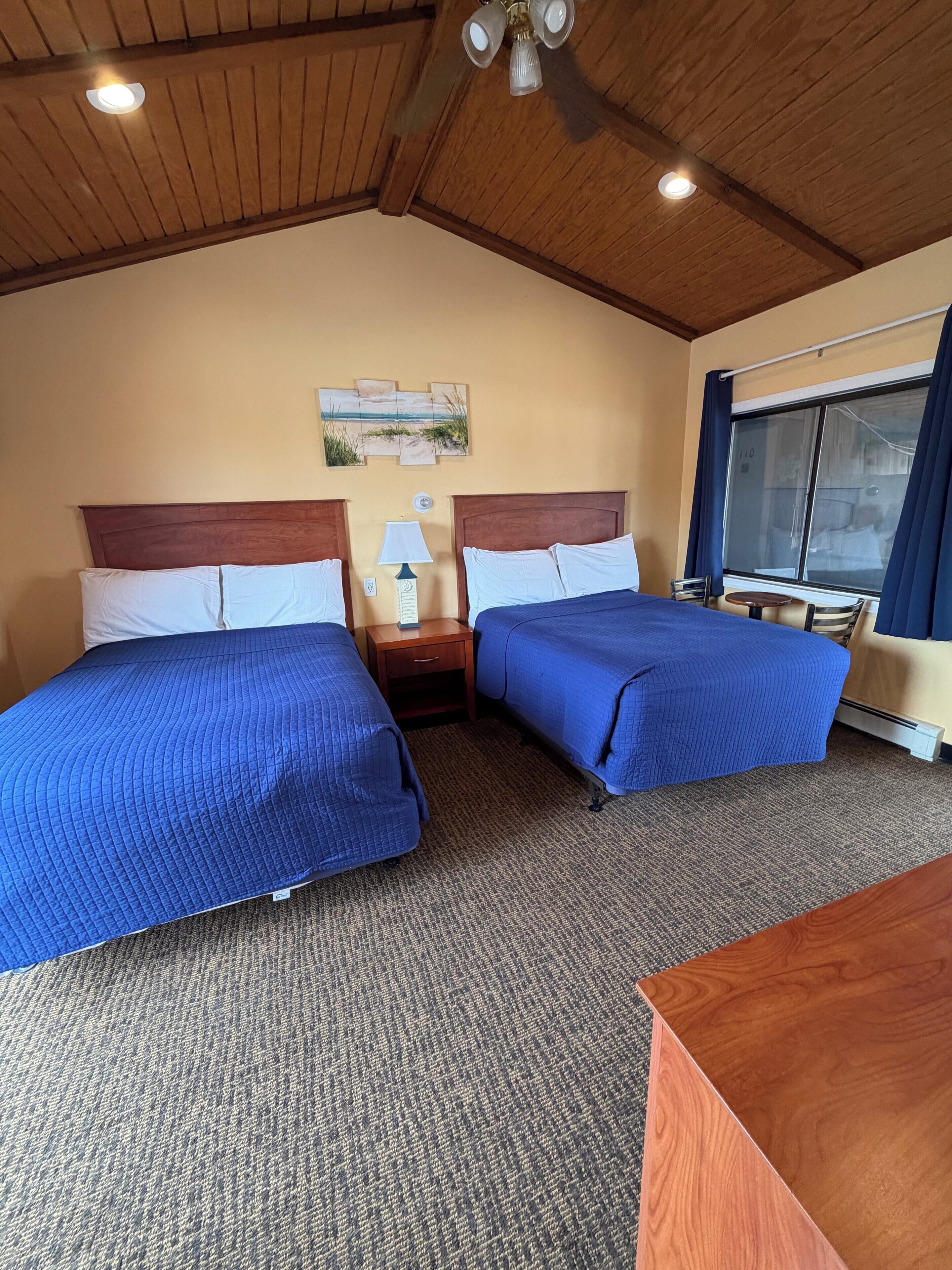 Habitación de hotel con dos camas, una mesita, una lámpara y una ventana con cortinas.