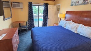 Habitación de hotel con cama, escritorio, silla, ventilador de techo y un cuadro en la pared.