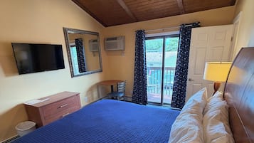 A bedroom with a large bed, a ceiling fan, a television, and a window with curtains.