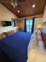 Un dormitorio con una cama grande, ventilador de techo, televisor y ventana con cortinas.