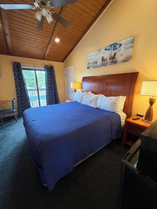 Habitación de hotel con una cama grande, techo de madera, un cuadro en la pared y una ventana con cortinas.