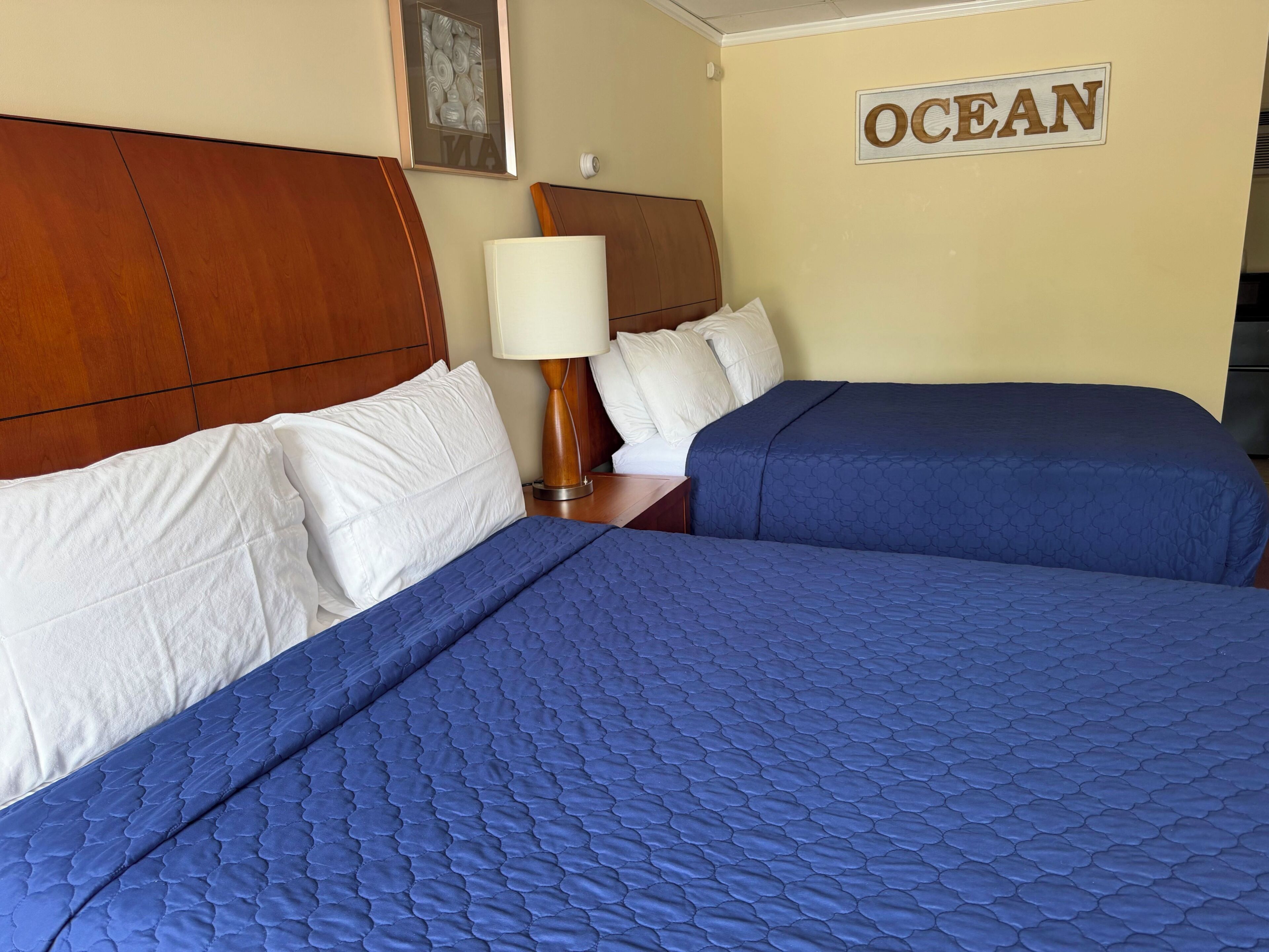 Habitación de hotel con dos camas, cabecera de madera, lámpara de pared y un cartel que dice 'OCEAN'.