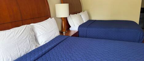 Habitación de hotel con dos camas, cabecera de madera, lámpara de pared y un cartel que dice 'OCEAN'.