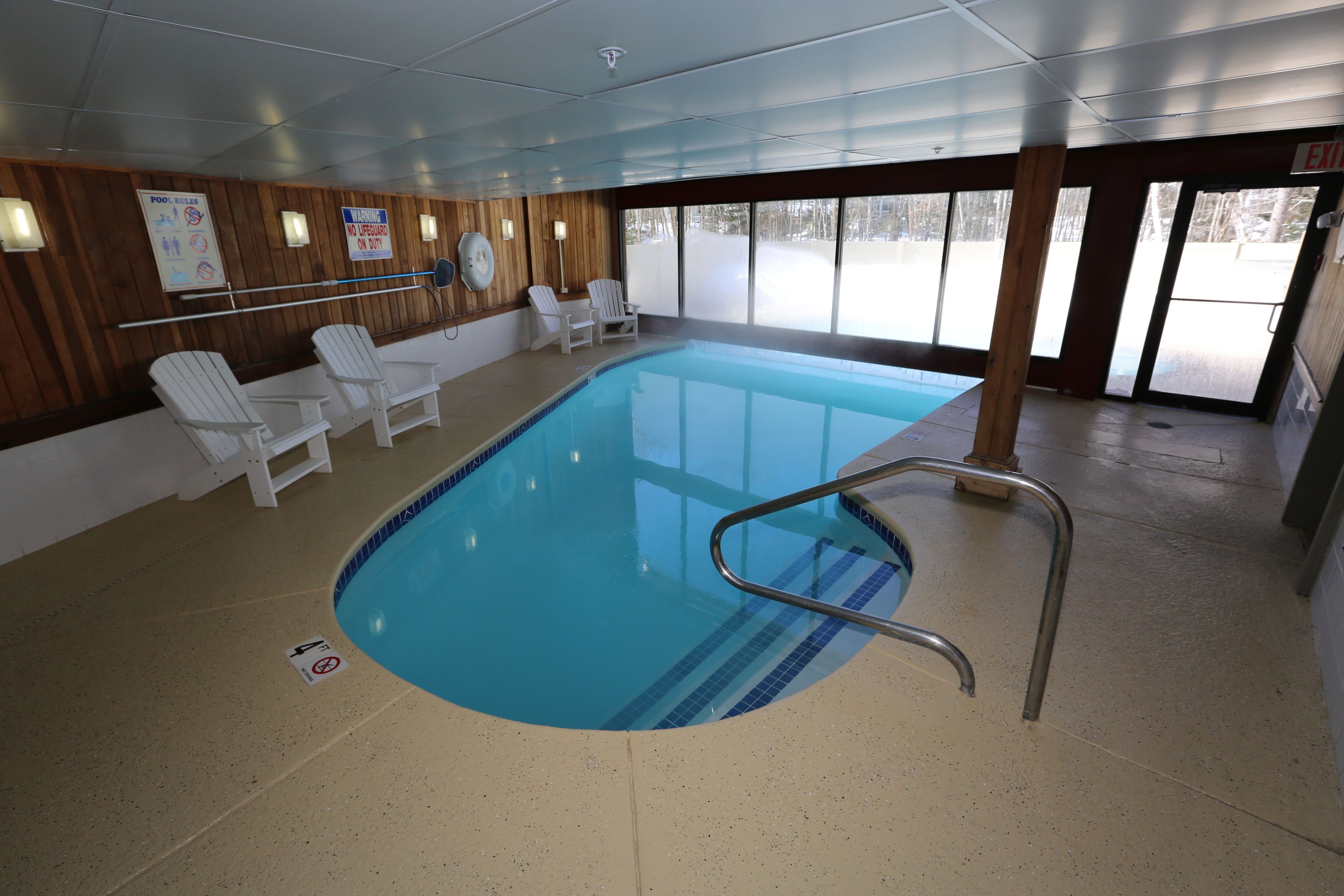 An indoor swimming pool with clear poolside areas, wooden paneling, and exit signs.