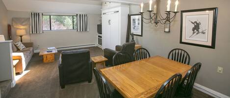 A cozy living room with a wooden dining table, black chairs, a sofa, and a TV.