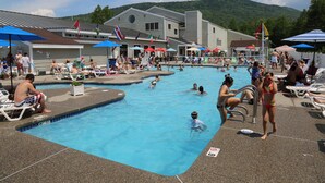A swimming pool area with multiple pools, lounge chairs, and umbrellas. - Black Bear Lodge (Waterville Valley)