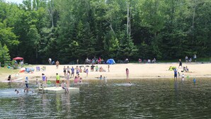 A lakeside beach with people swimming and sunbathing, surrounded by dense forest. - Black Bear Lodge (Waterville Valley)
