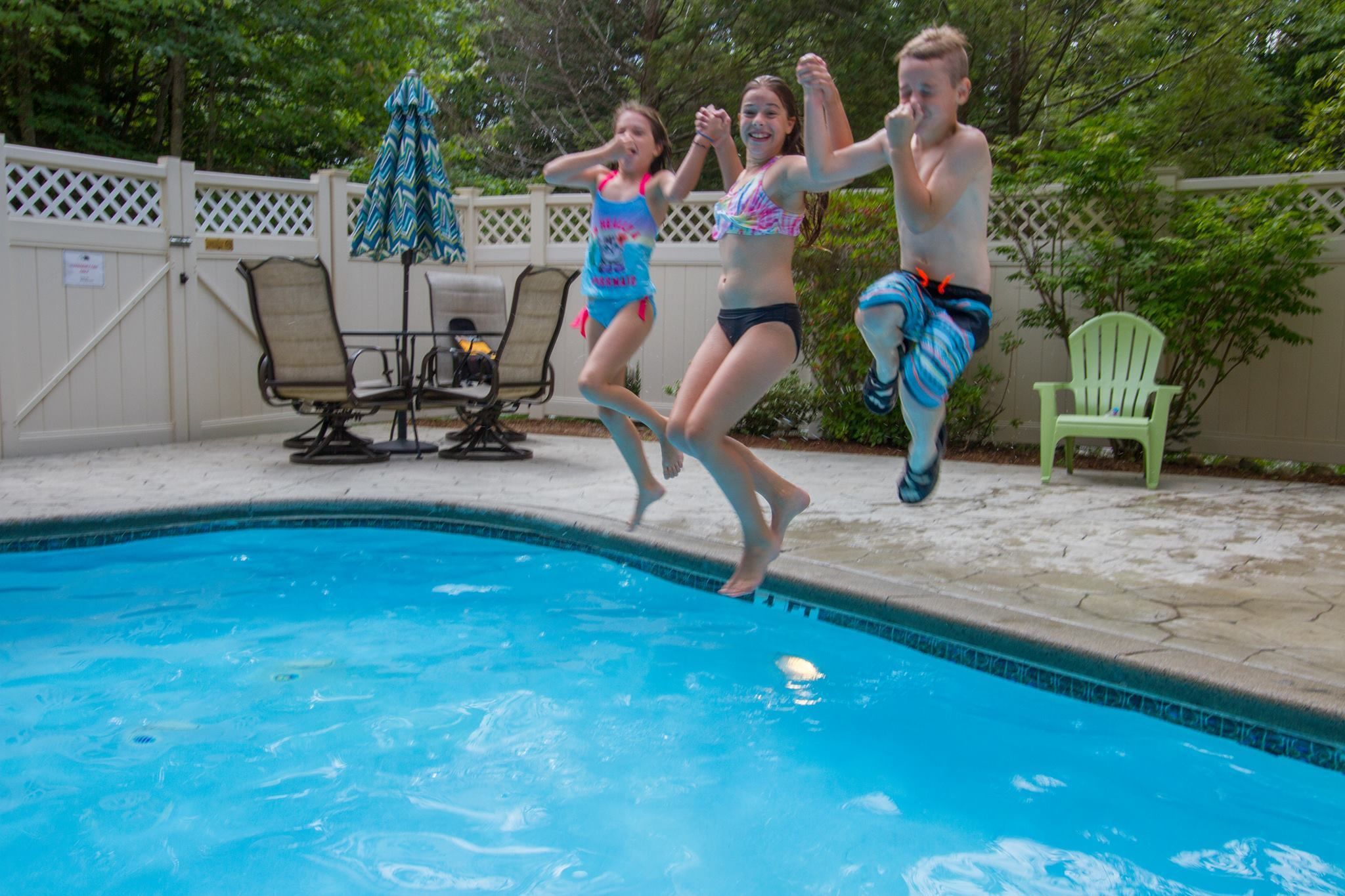 A swimming pool with a white fence, lounge chairs, and a green chair.