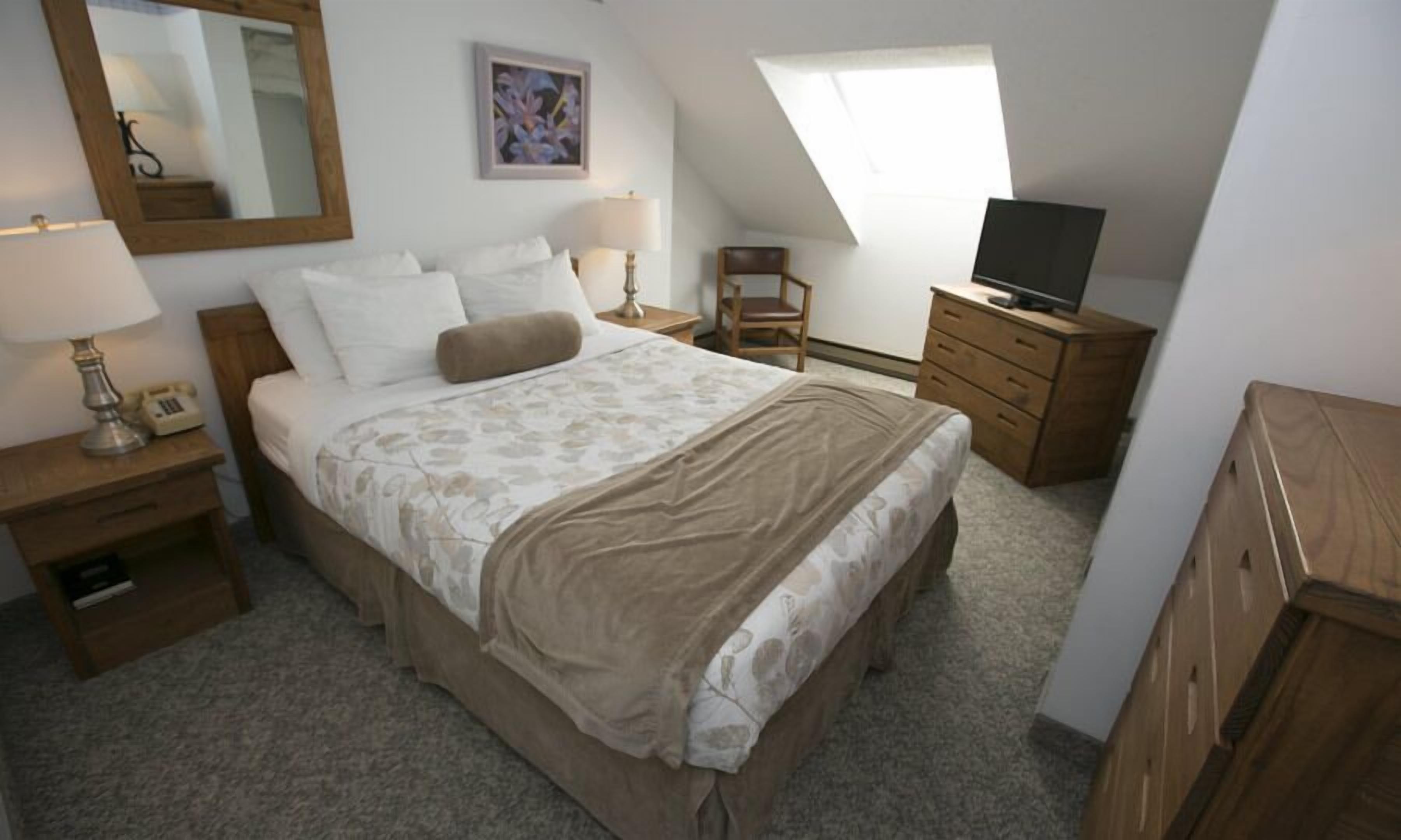 Ein Schlafzimmer mit Bett, Nachttisch, Schminktisch, Fernseher, Stuhl, Spiegel und einem Bild an der Wand.