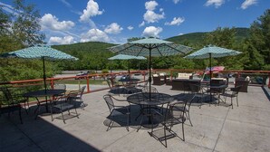 An outdoor patio with tables and chairs, surrounded by red railings, and featuring large patterned umbrellas. - Black Bear Lodge (Waterville Valley)