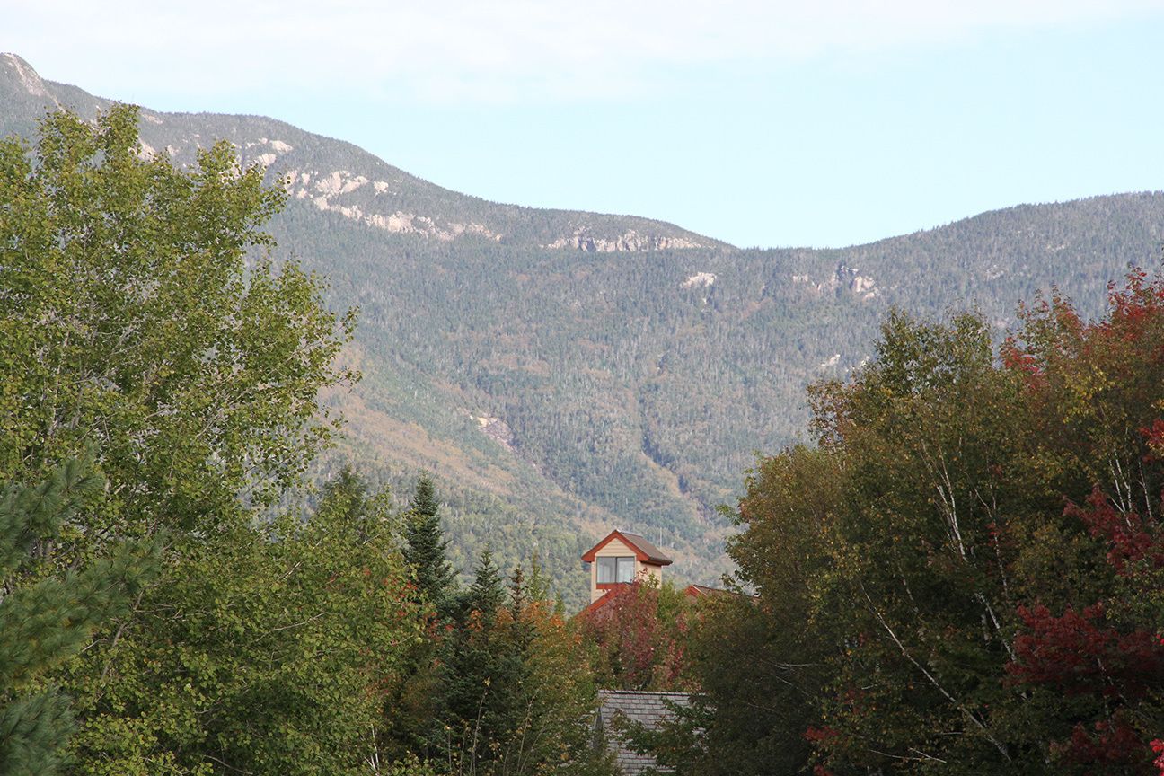 A mountain cabin with a red roof nestled among trees, surrounded by forested hills.