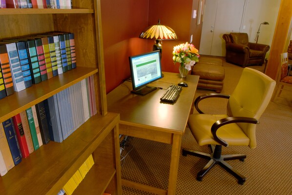 A room with a wooden desk, a computer, a lamp, a chair, and a bookshelf with books.