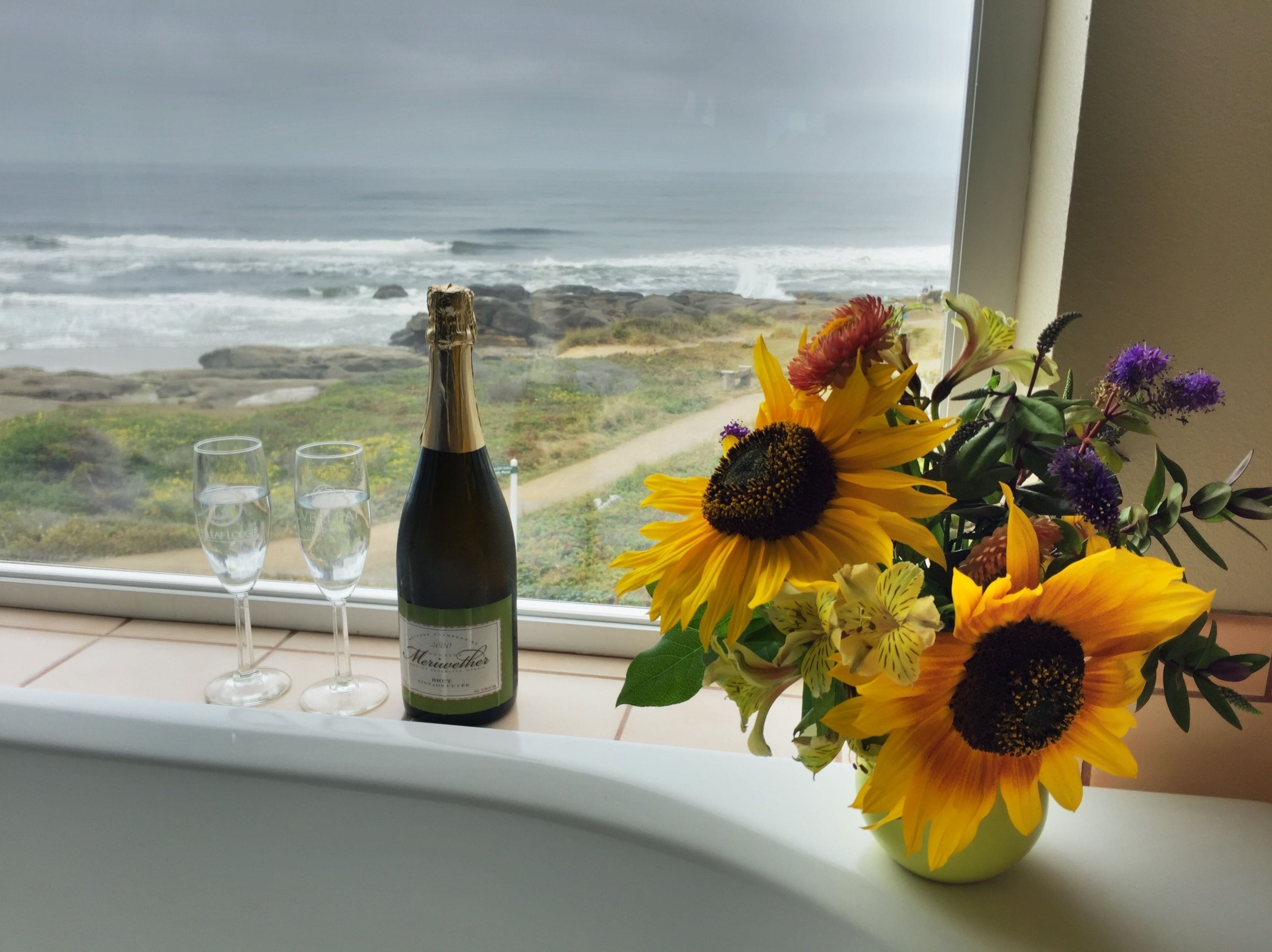 Una botella de vino y tres copas sobre un alféizar con vista al océano.