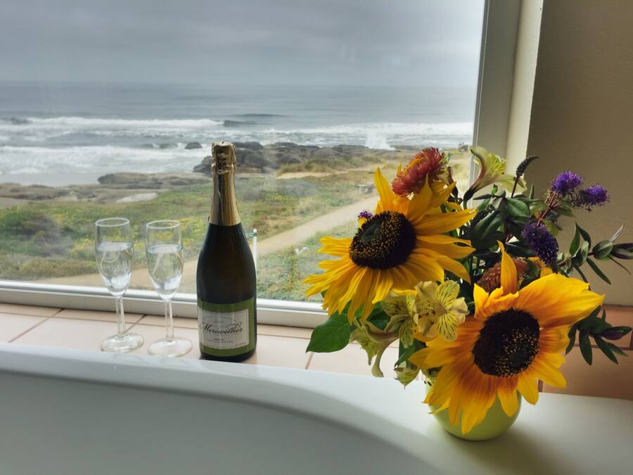 Una botella de vino y tres copas sobre un alféizar con vista al océano.
