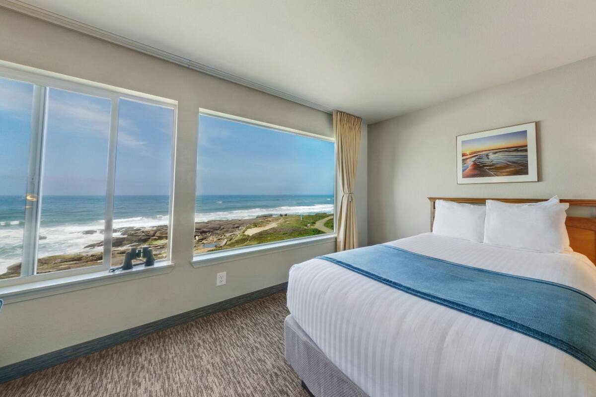A hotel room with a large bed, a view of the ocean, and a painting on the wall.
