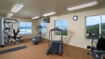 A gym with cardio machines, a treadmill, and a TV screen.