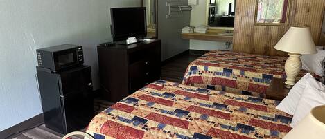 A hotel room with two beds, a desk with a television, a mirror, and a lamp.