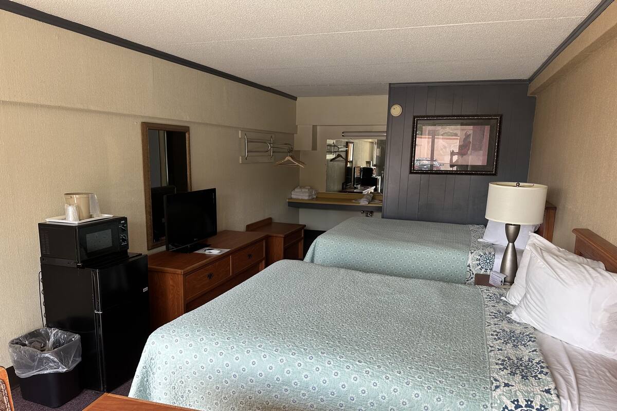 Une chambre d’hôtel avec deux lits, un bureau, une télévision, un miroir et une salle de bain.