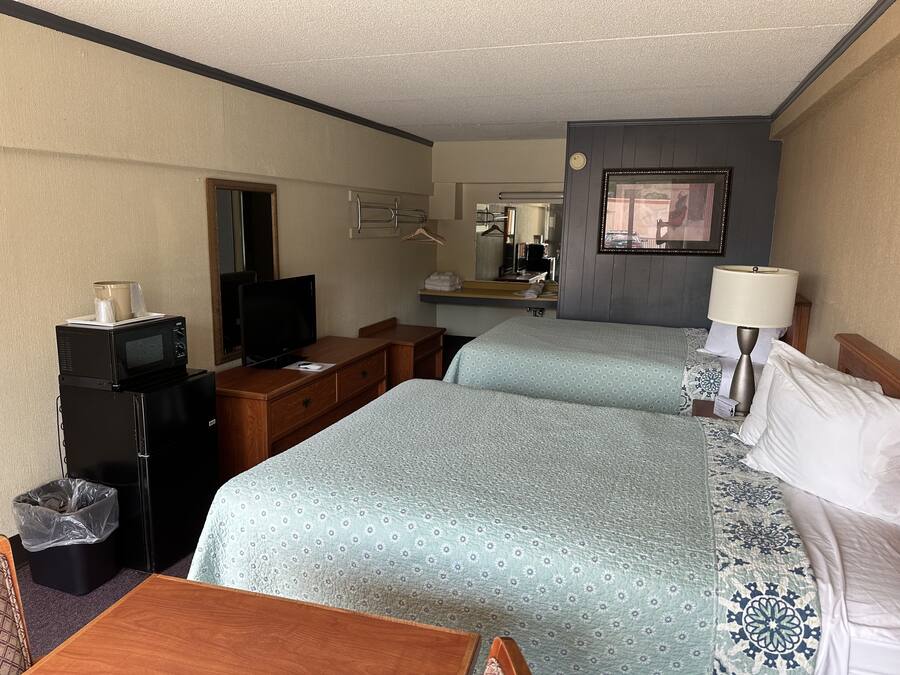 A hotel room with two beds, a desk, a television, a mirror, and a bathroom.