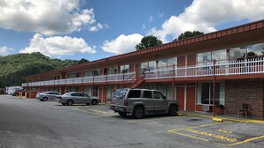 A motel with a parking lot, a red building, and a white fence. - Daniel Boone Motor Inn (Pikeville)