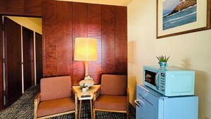 A hotel room with a wooden panel wall, a sofa, a small table with a lamp, a microwave, and a framed picture on the wall. - Curly Redwood Lodge (Crescent City)