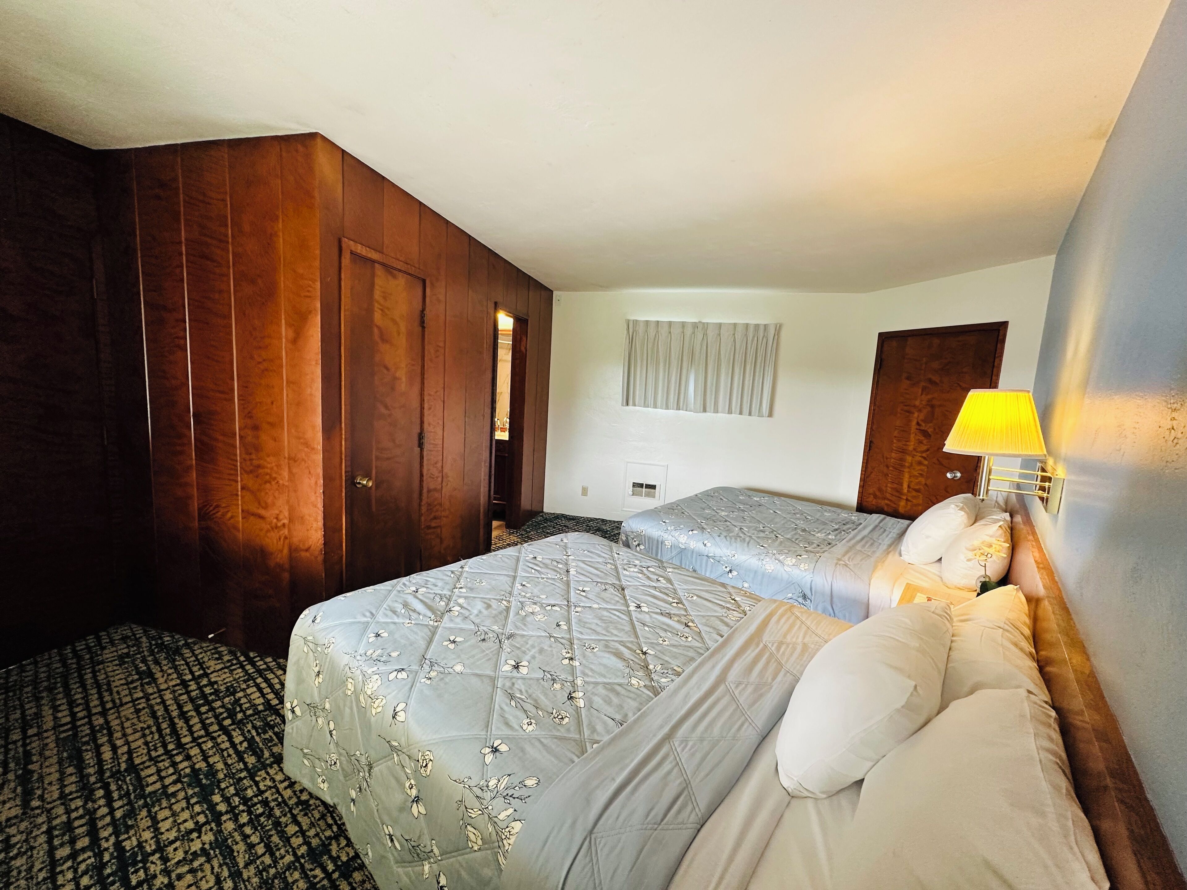 Ett hotellrum med två sängar, en garderob, ett fönster med gardiner och en sänglampa.