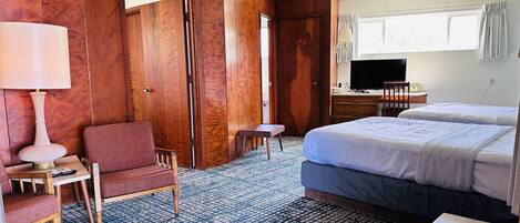 A hotel room with a bed, a desk with a lamp, a chair, a TV, and a window with curtains.