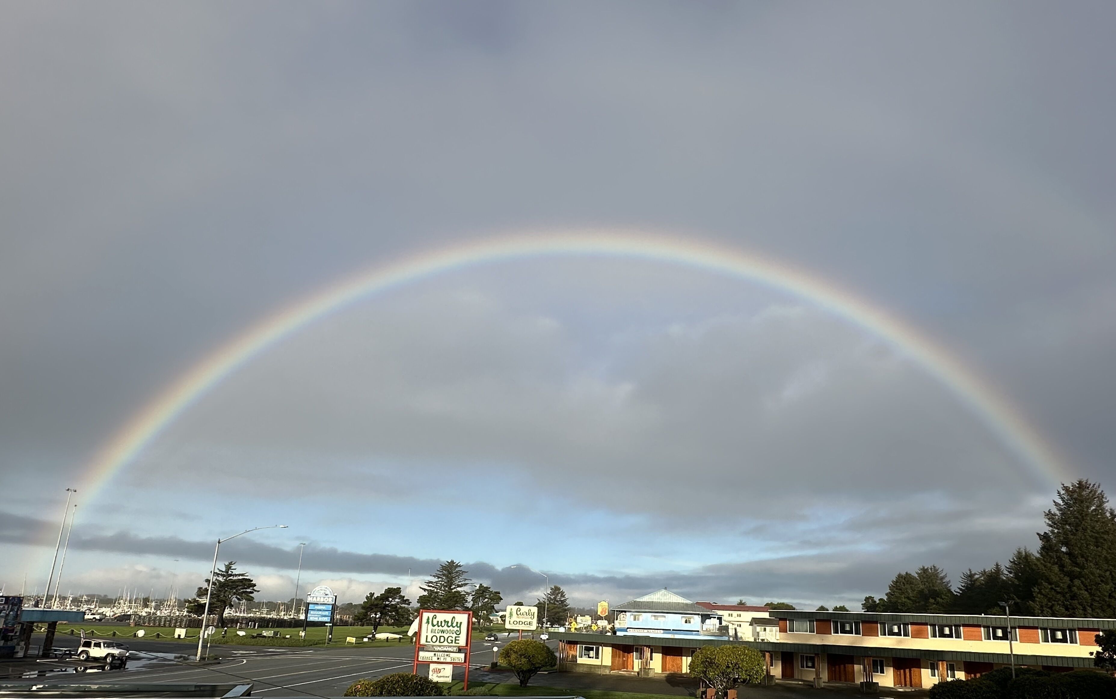A rainbow over a marina with a sign for Curly Lodge.