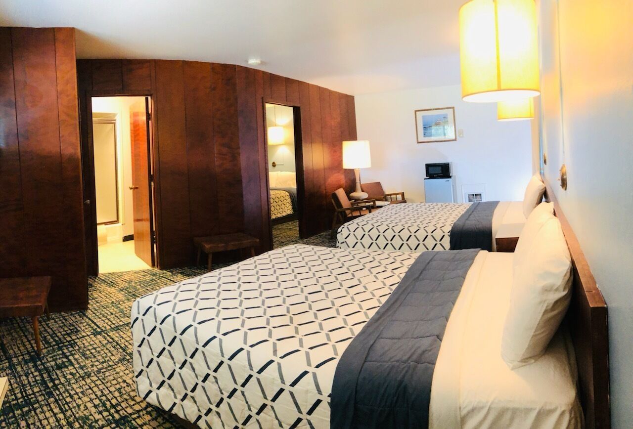A hotel room with two beds, a desk, a chair, and a lamp.