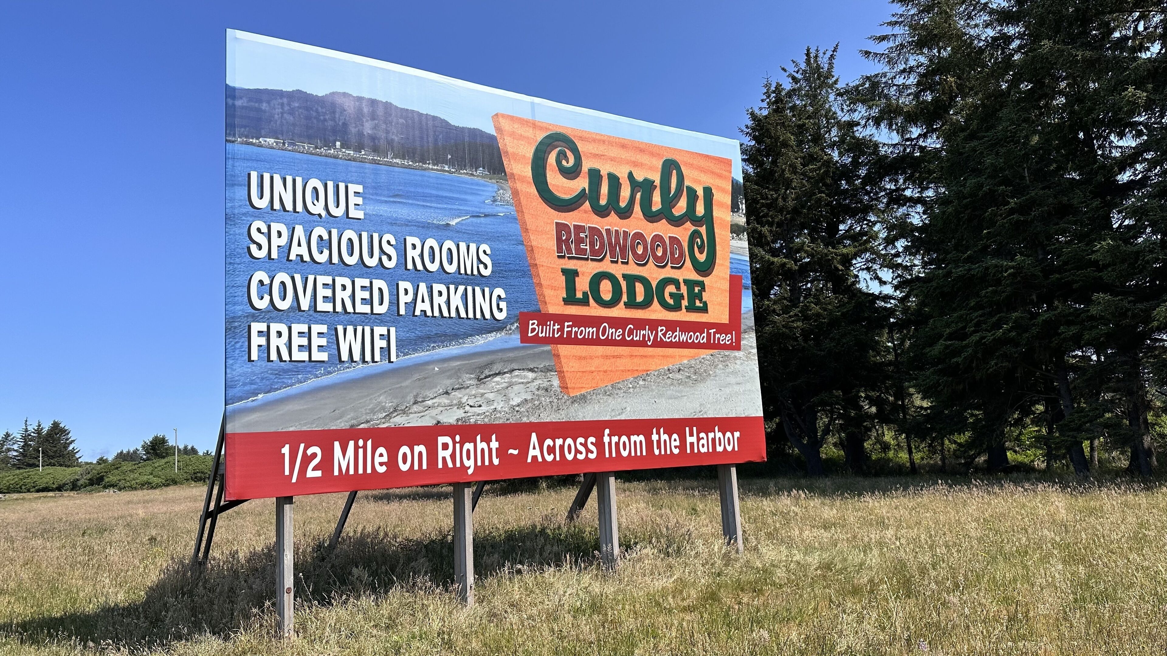 Eine Werbetafel für das Curly Redwood Lodge mit Annehmlichkeiten wie großzügigen Zimmern, überdachter Parkplatz und kostenlosem WLAN.