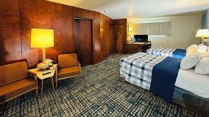 A hotel room with a wooden wall, a desk with a lamp, a bed with a checkered bedspread, and a television. - Curly Redwood Lodge (Crescent City)