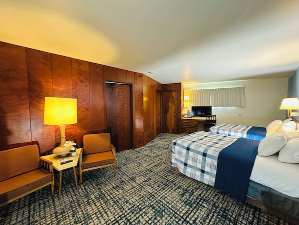 Una habitación de hotel con una pared de madera, un escritorio con una lámpara, una cama con colcha a cuadros y un televisor.