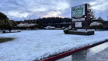 Señal del Curly Redwood Lodge con aviso de habitaciones disponibles, asientos exteriores y un estacionamiento cubierto de nieve.