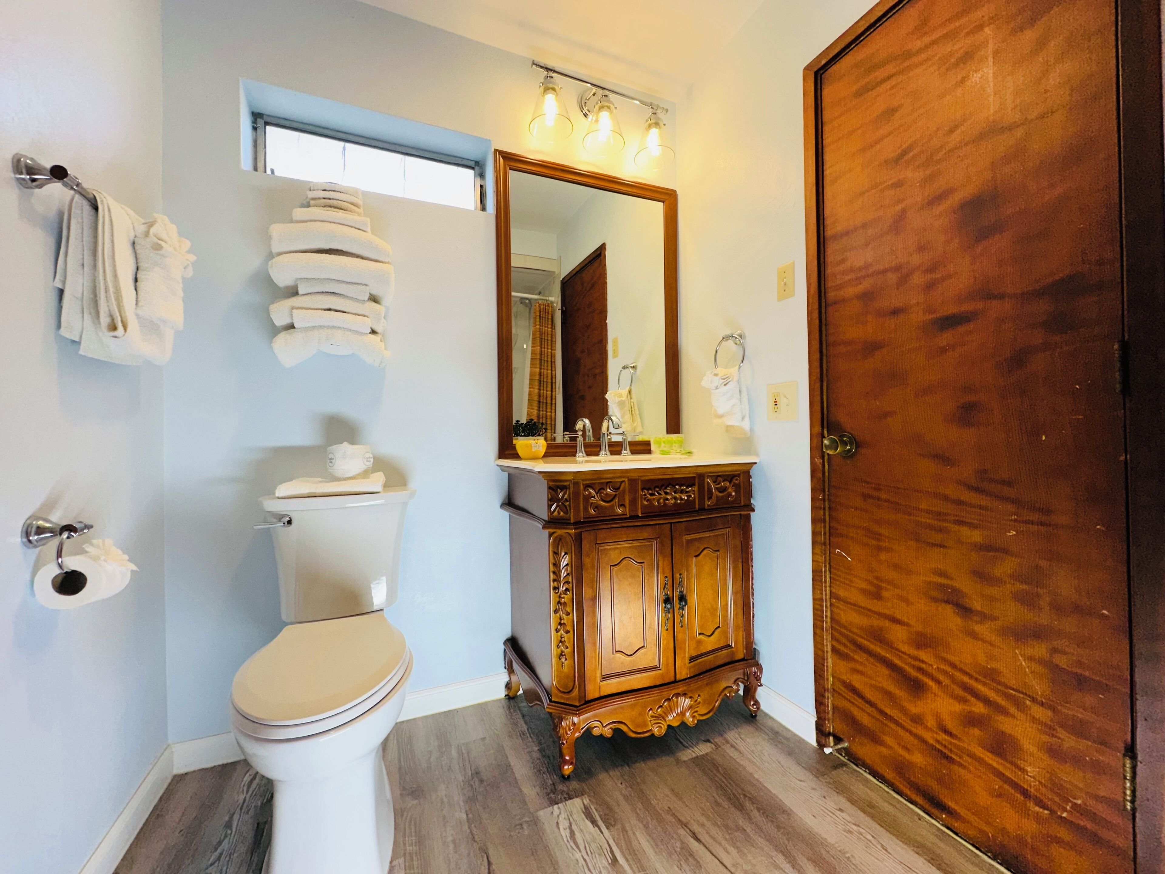 A bathroom with a toilet, sink, mirror, and wooden cabinet.