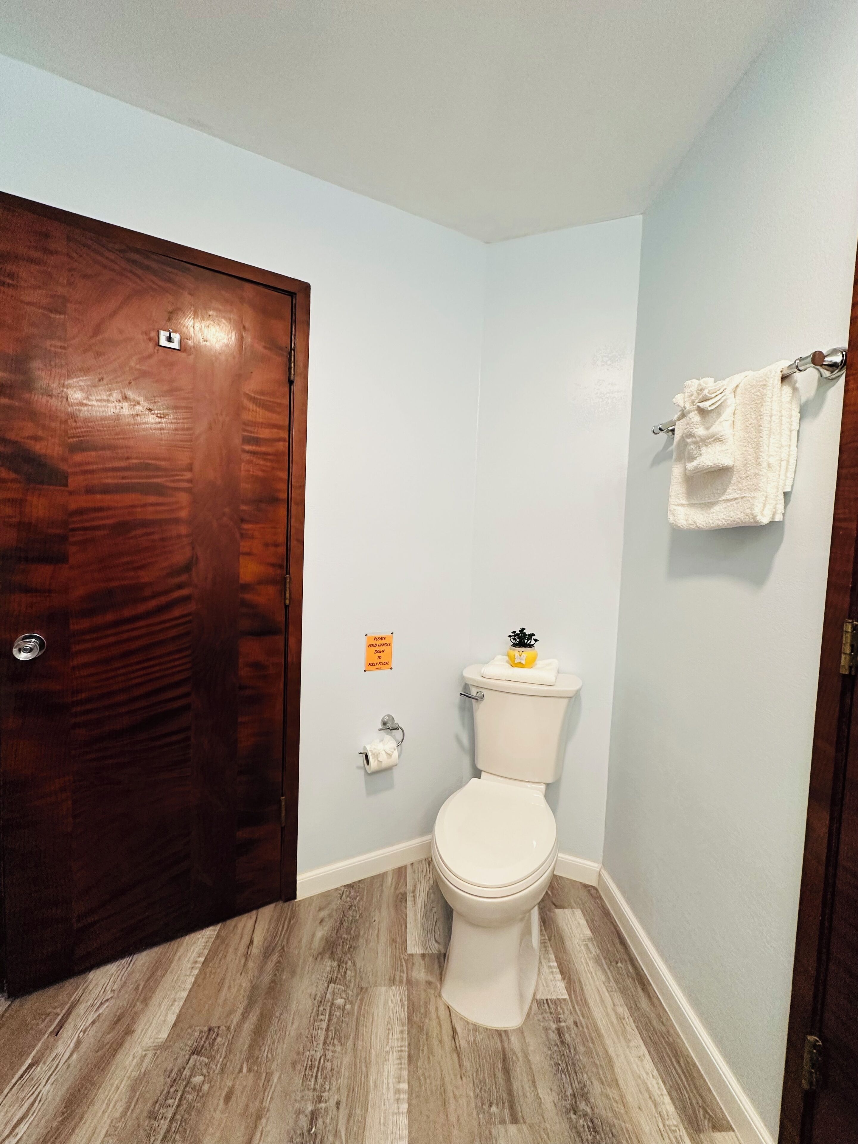 Un baño con puerta de madera, un inodoro, un perchero para toallas y un dispensador de papel higiénico.