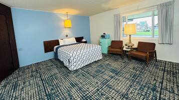 A hotel room with a bed, a desk, two chairs, a lamp, a microwave, and a view of the outside.