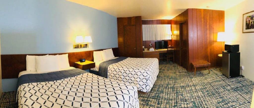 A hotel room with two beds, a desk, a chair, a TV, and a desk lamp.