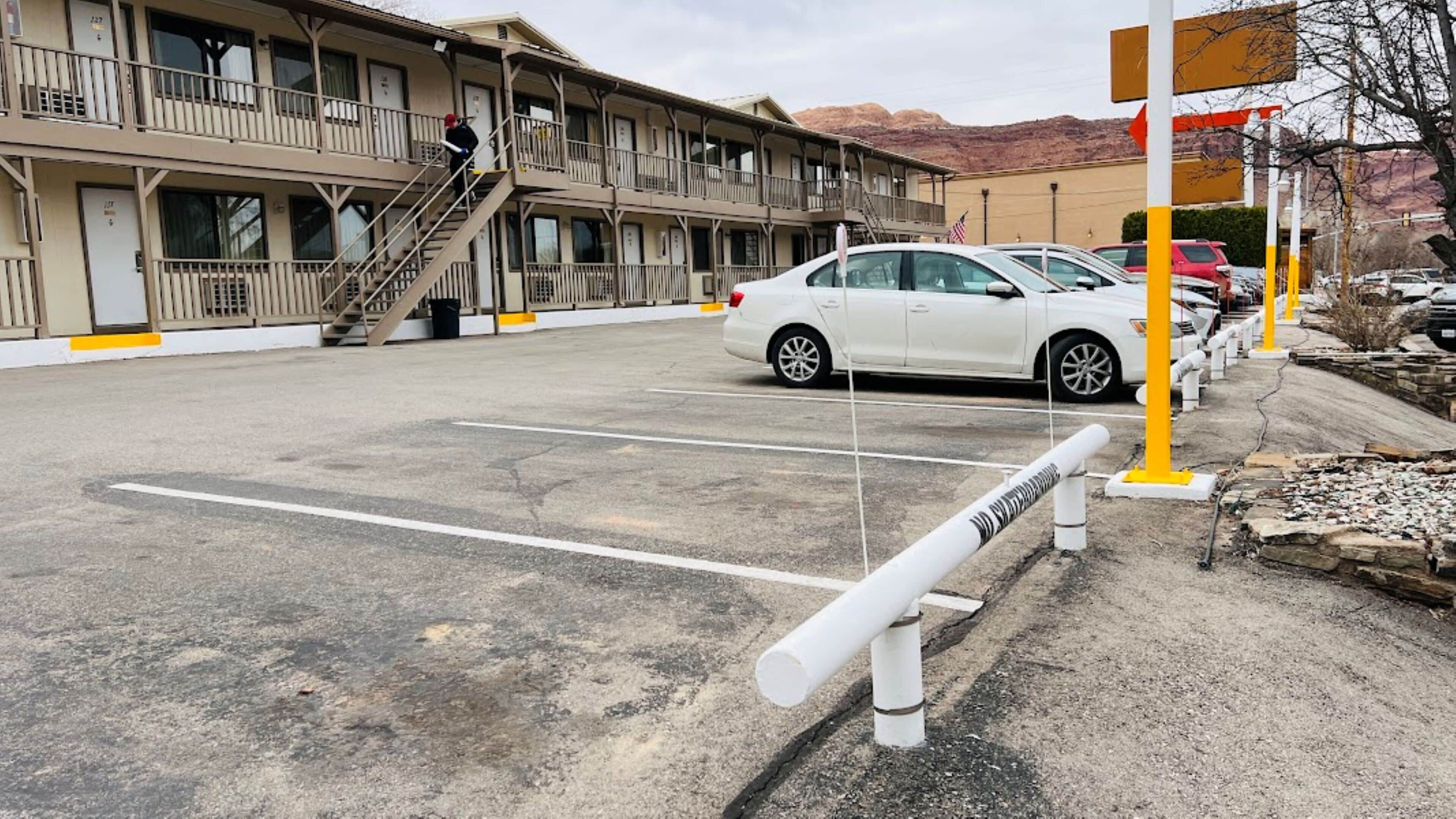 Un motel à plusieurs étages, doté d’un parking, d’un escalier et offrant une vue sur les montagnes en arrière-plan.